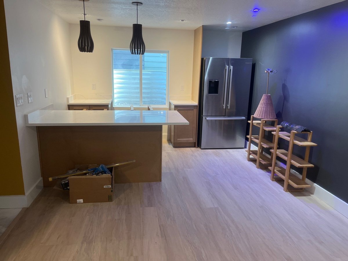 RemodelCo basement kitchenette installation in Daybreak, UT featuring a quartz island, custom cabinetry, and stainless steel refrigerator.
