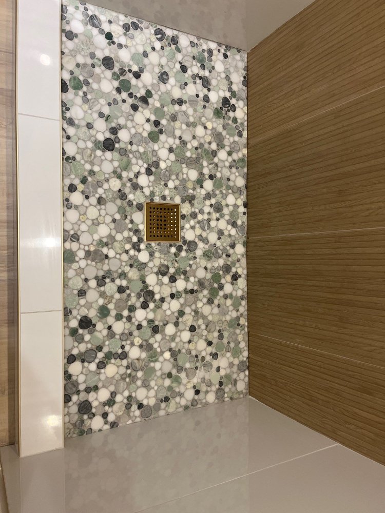 Close-up of pebble tile shower base and premium drain fixture by RemodelCo in Daybreak, UT.-optimized
