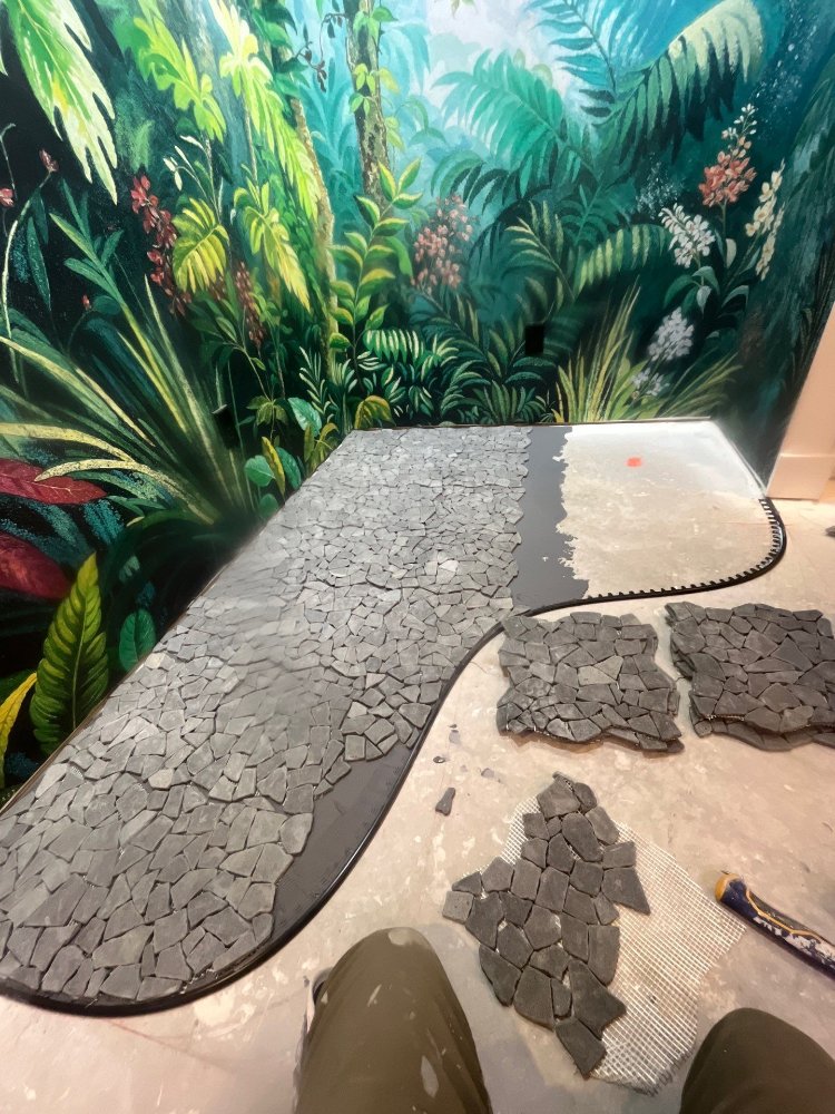 Custom black mosaic tile installation in progress beneath tropical wall mural during a RemodelCo basement finish in Daybreak, UT-optimized