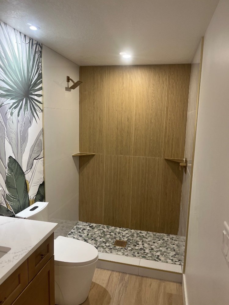 Custom walk-in shower showcasing wood-look accent tile and pebble flooring in a RemodelCo project in Daybreak, UT.-optimized