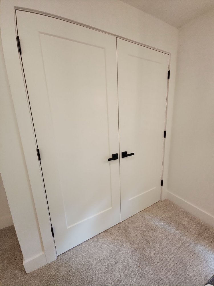 Double white closet doors with matte black handles installed by RemodelCo during a basement finish in Daybreak, UT.-optimized