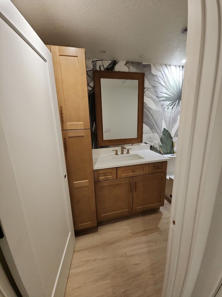 RemodelCo basement finish bathroom vanity with custom wood cabinetry, quartz countertop, and botanical wallpaper in Daybreak, UT-optimized