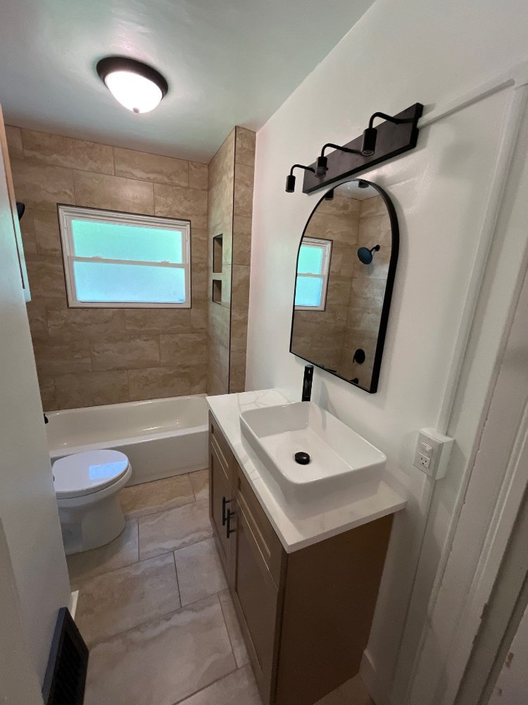 Bathroom remodel by RemodelCo in Salt Lake City, UT featuring an arched mirror, vessel sink vanity, and tiled bathtub surround.-optimized