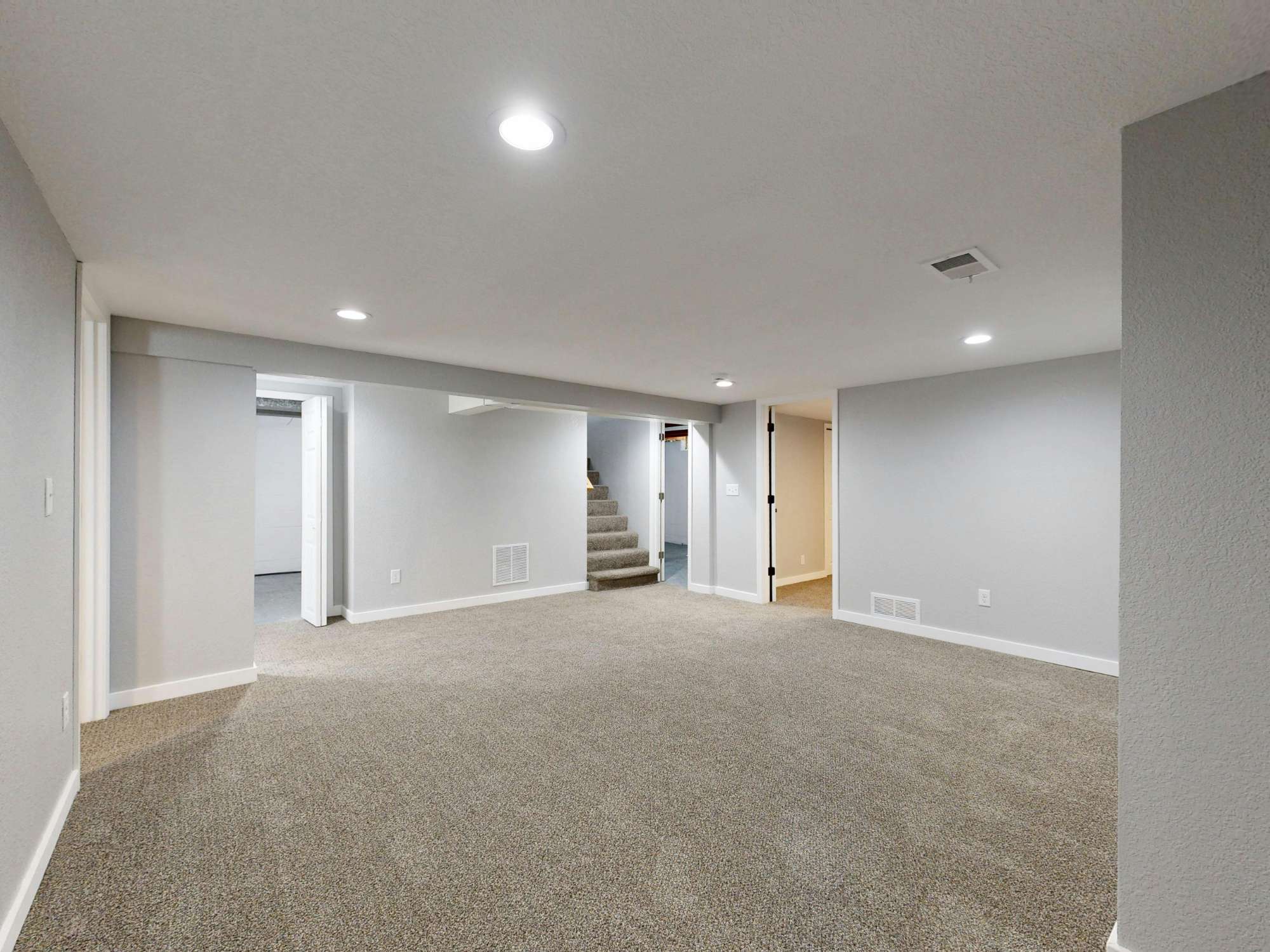 Open finished basement with plush carpeting and multiple room access points in a Sandy, UT basement remodel by RemodelCo stock-optimized