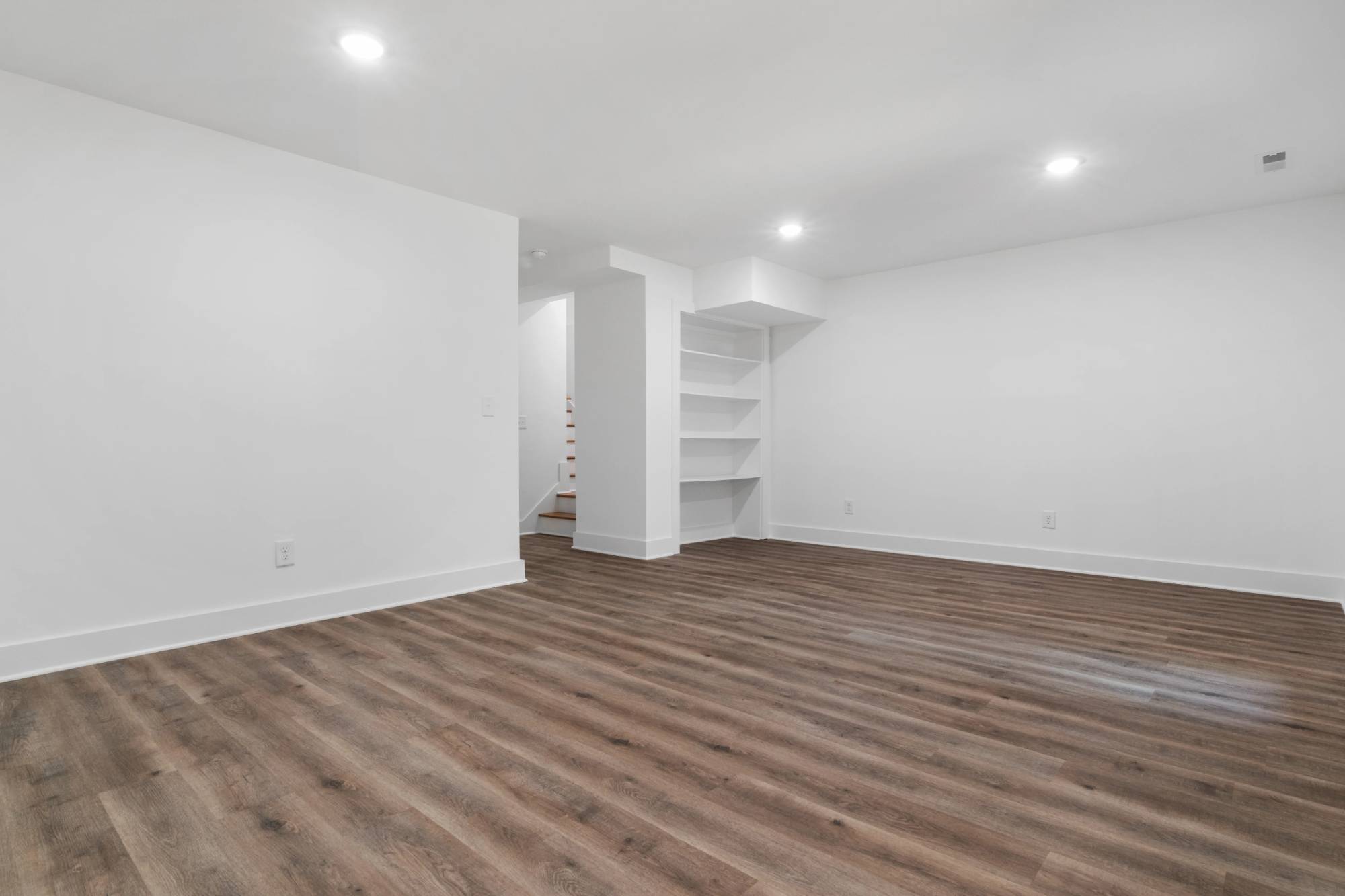Unfurnished basement living area with built-in shelving and luxury vinyl flooring in a Sandy, UT basement remodel by RemodelCo s-optimized