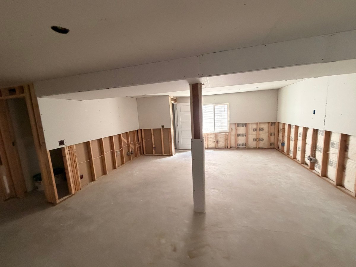 Basement finishing project during drywall installation with exposed framing and insulation along the lower walls.