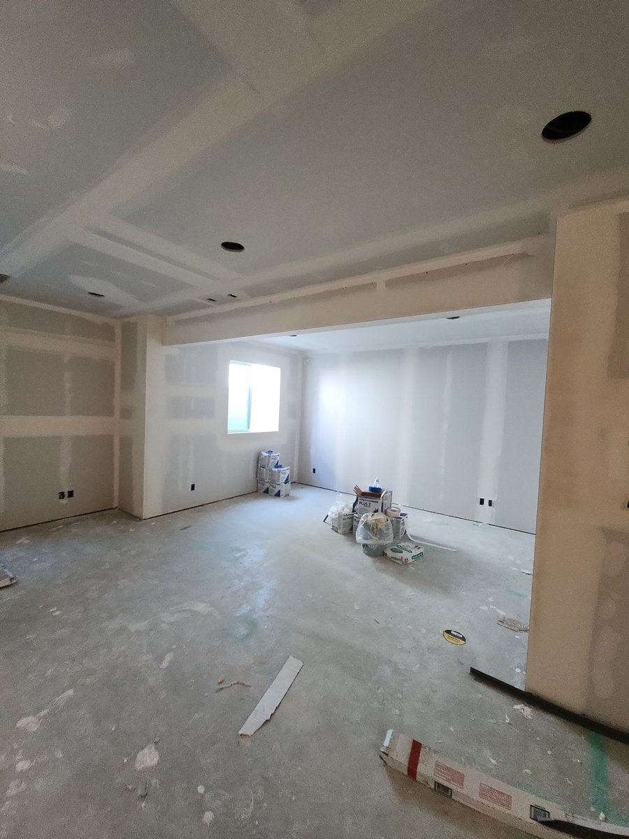 Open basement living area during painting and finishing with primed walls, recessed lighting, and construction supplies.