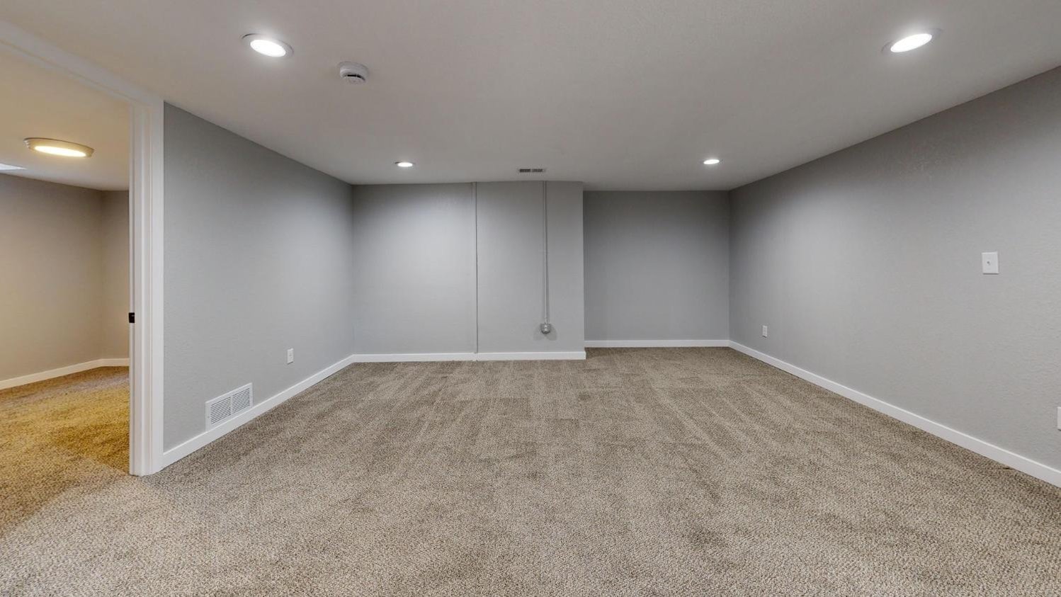 Large basement recreation room with plush carpeting and modern finishes in a Sandy, UT basement remodel by RemodelCo 