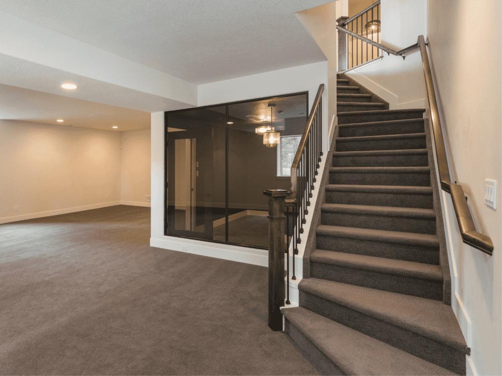 Modern basement staircase with glass-enclosed room and open living area in a Sandy, UT basement remodel by RemodelCo