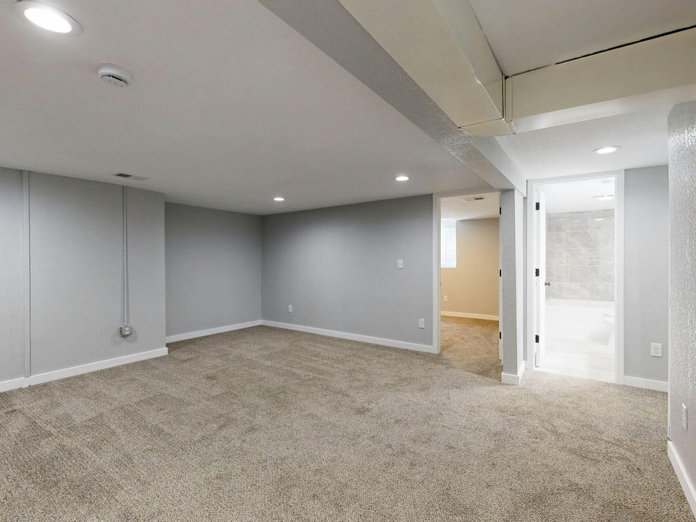 Open basement recreation room with modern finishes and plush carpeting in a Sandy, UT basement renovation by RemodelCo