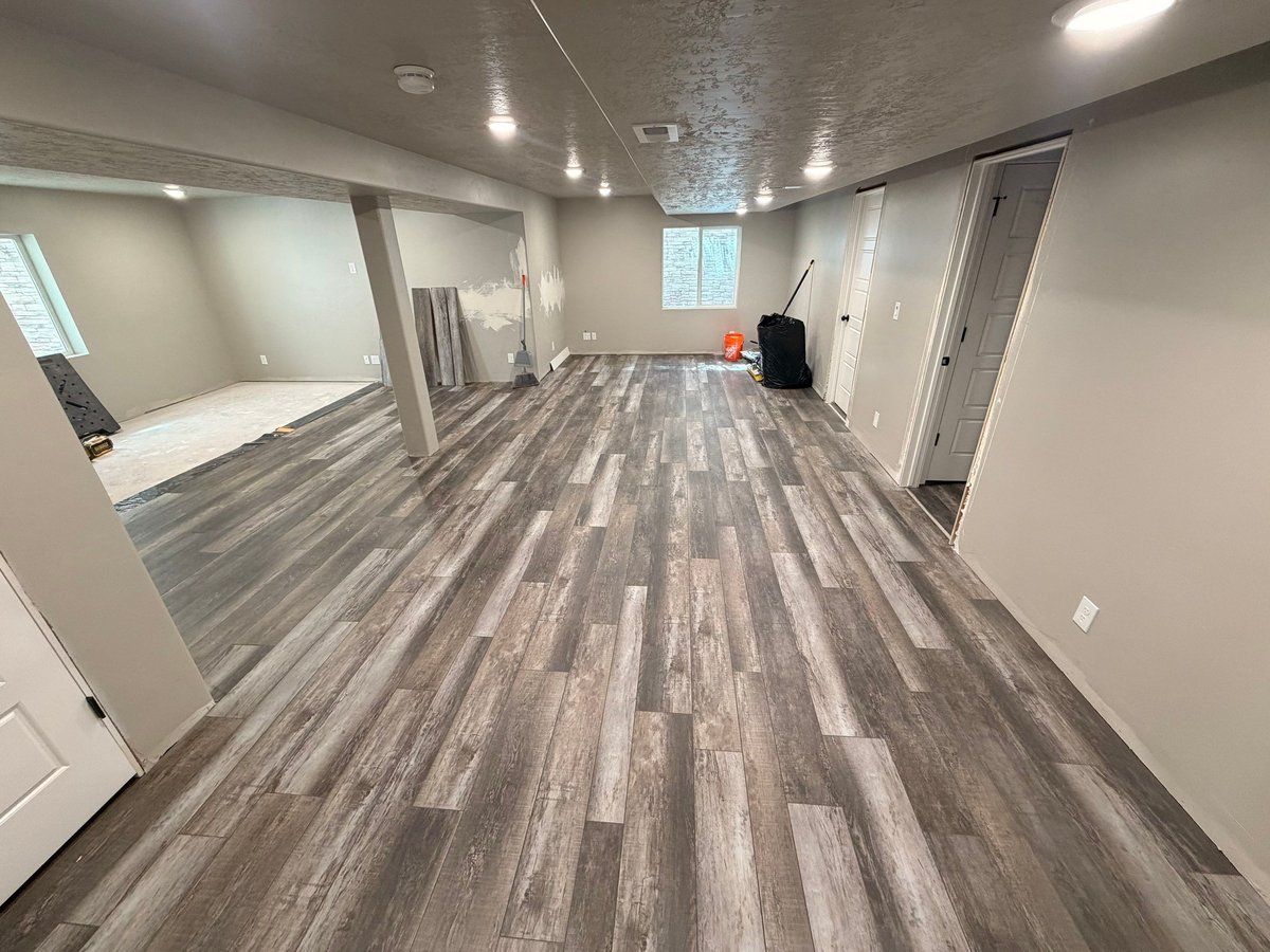 Finished basement living area with gray wood-look flooring, recessed lighting, neutral walls, and white doors.