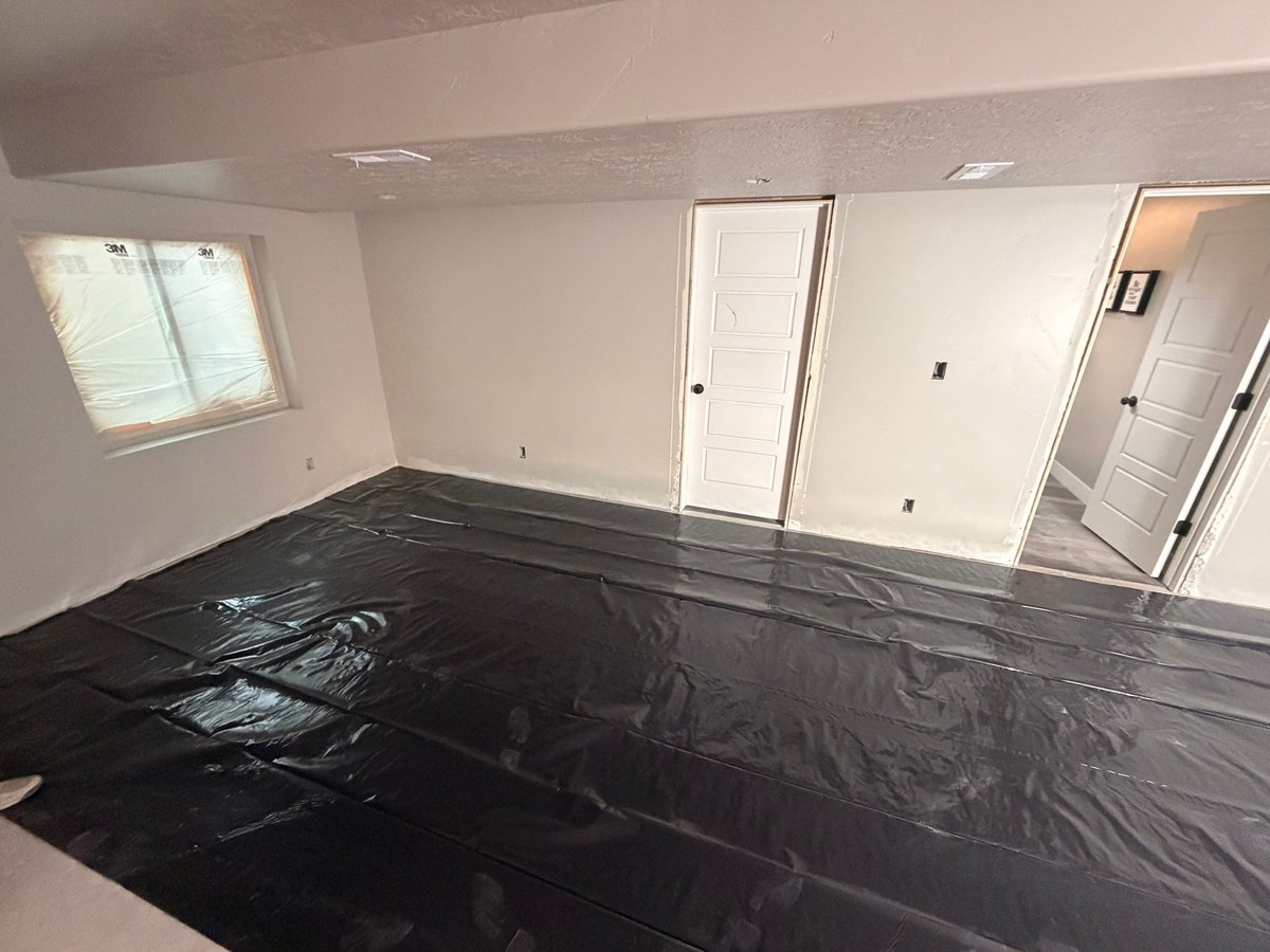 Basement renovation in progress with protective floor covering, painted walls, and interior doors installed.