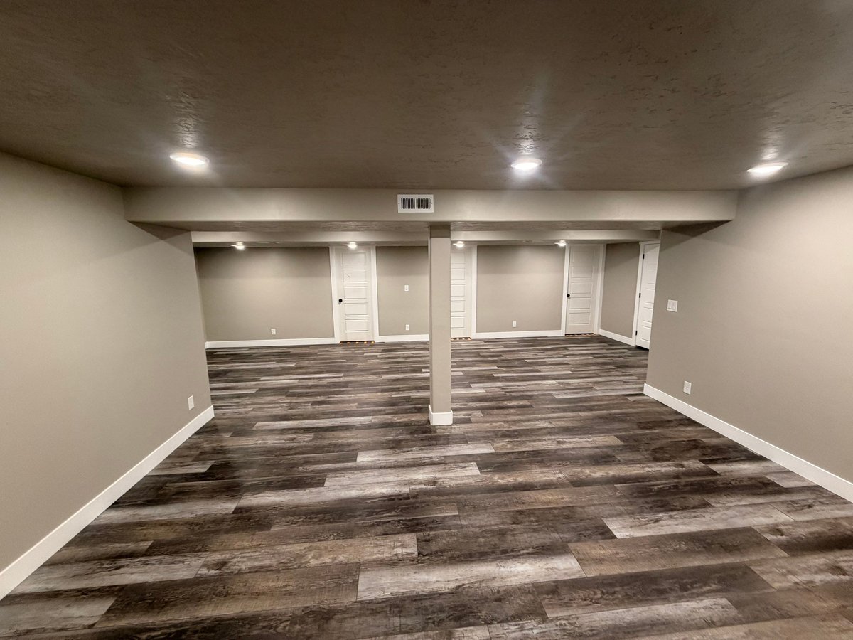 Finished basement living area with gray wood-look flooring, recessed lighting, neutral walls, and white doors.