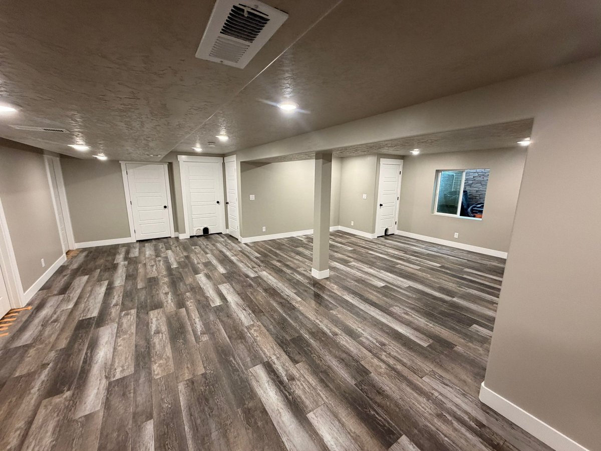 Finished basement living area with gray wood-look flooring, recessed lighting, neutral walls, and white doors.