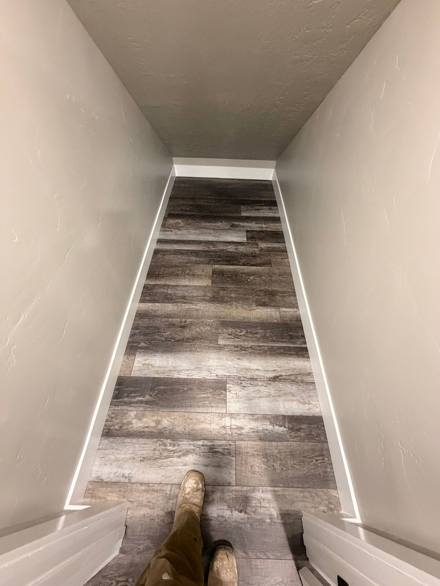 Finished basement living area with gray wood-look flooring, recessed lighting, neutral walls, and white doors.