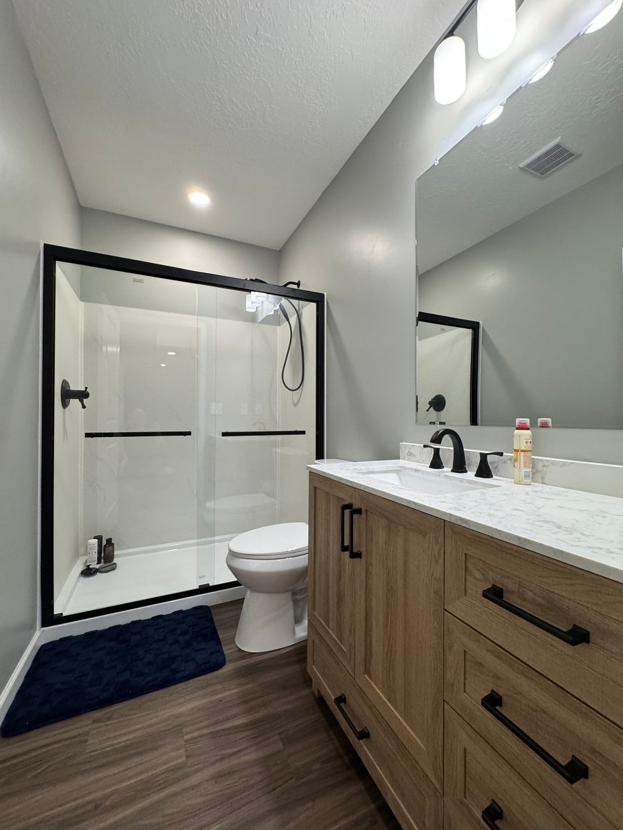 Finished basement bathroom with glass shower, wood vanity, and black fixtures.