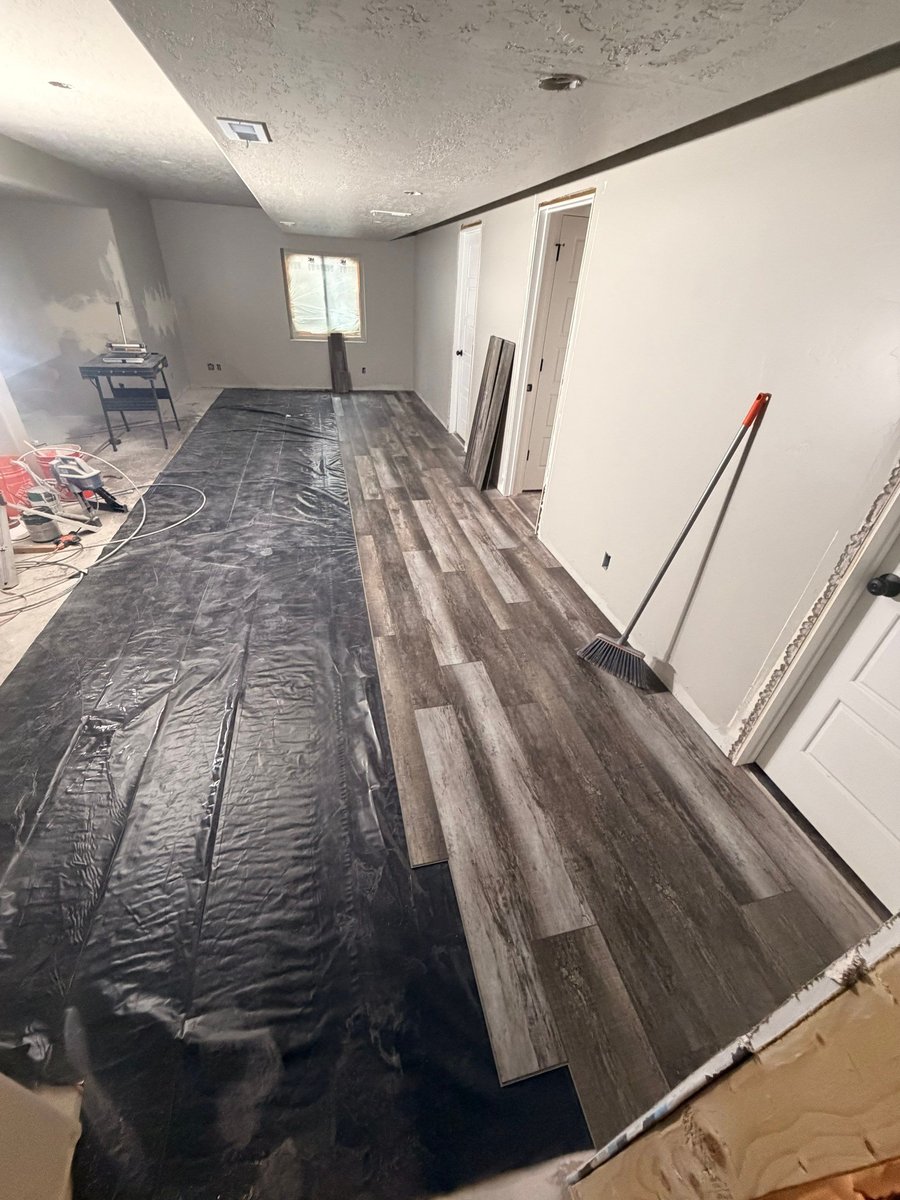 Finished basement living area with gray wood-look flooring, recessed lighting, neutral walls, and white doors.