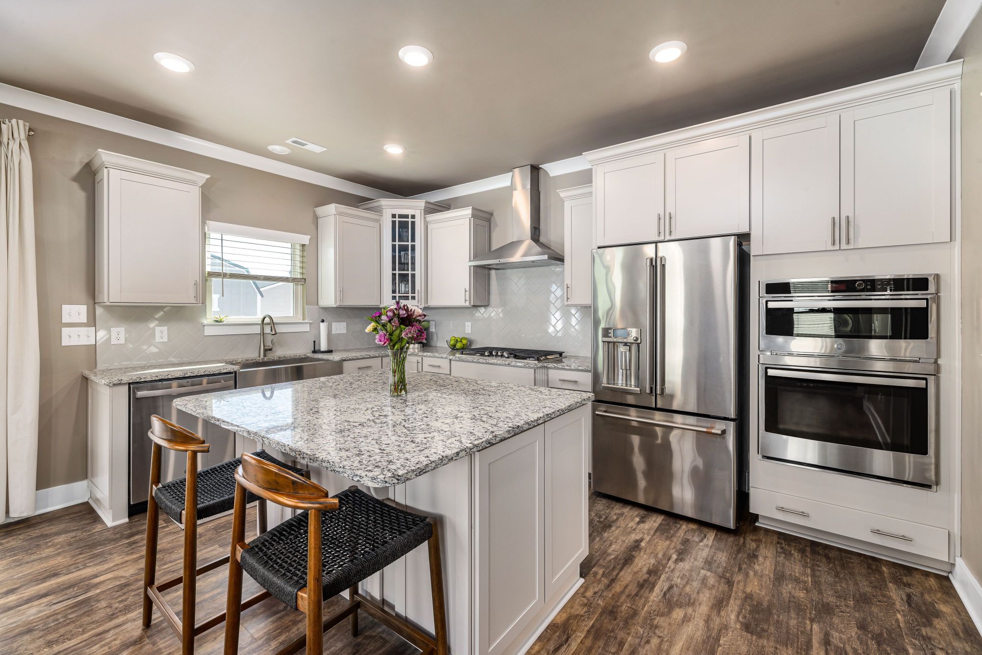 Modern kitchen with granite countertops, wood look flooring, double ovens, and kitchen island 